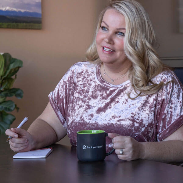 A smiling woman in an office actively listening and making notes.