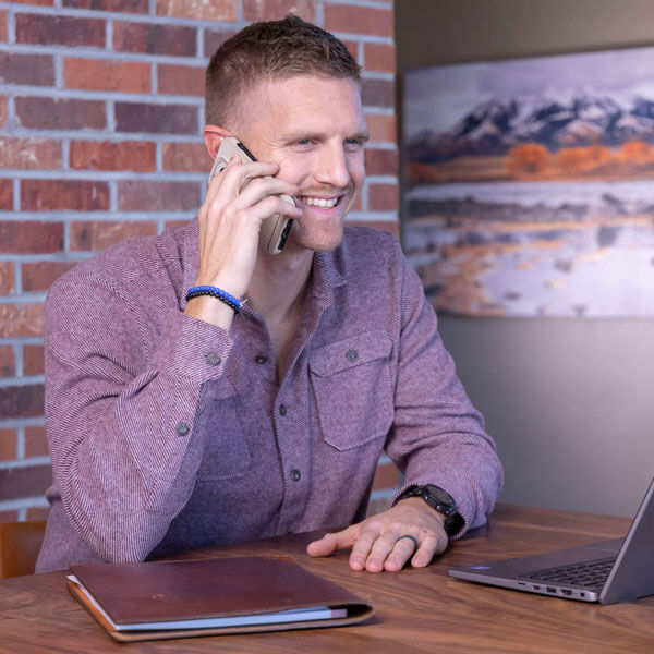 A smiling man on a phone conversation in an office.