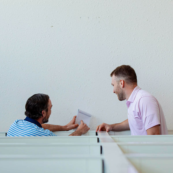 Two men in an office looking at a notepad from their cubicles.